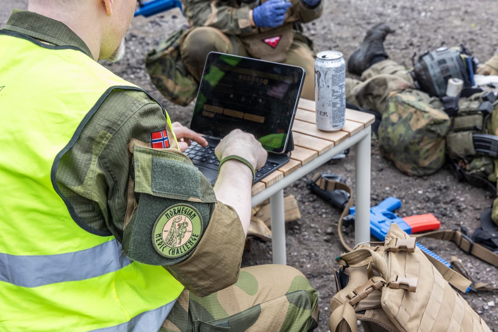 An NMC judge scoring on a tablet while a team treats a casualty in the background