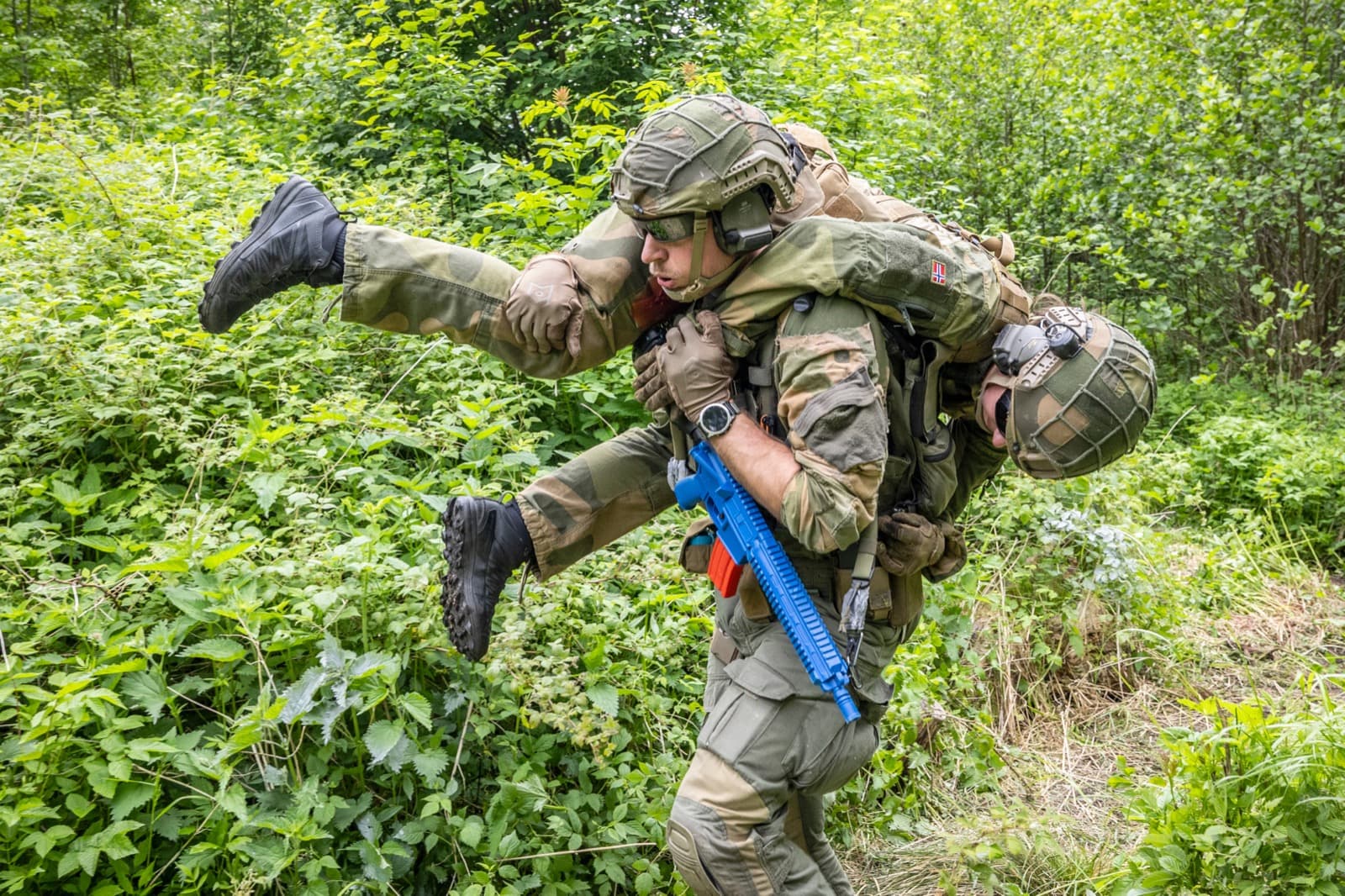 A medic carrying a casualty in a fireman's carry through rough terrain